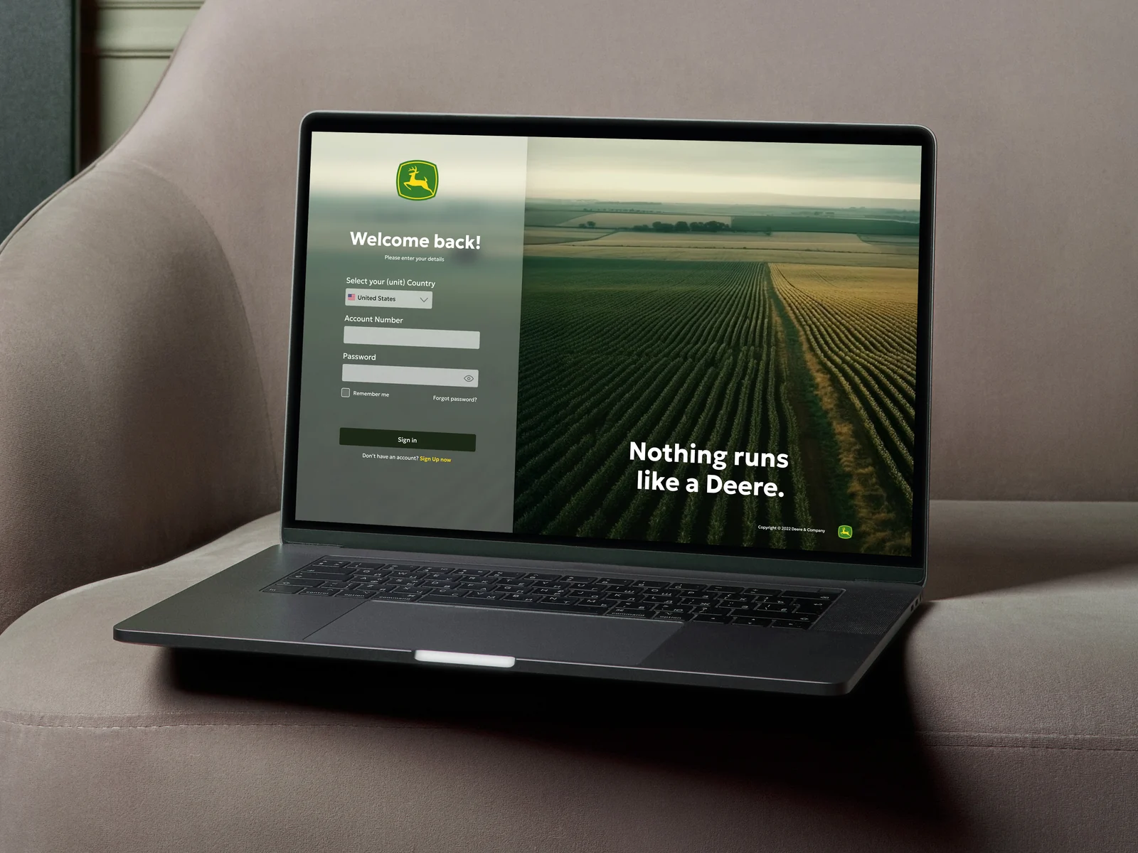 Laptop on a couch showing the John Deere customer portal login screen: “Welcome back!” and “Nothing runs like a Deere.”